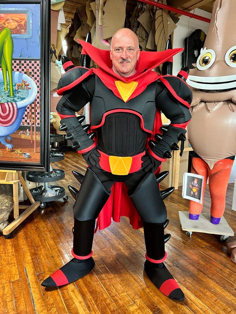 A man in a superhero costume is standing in front of a painting.