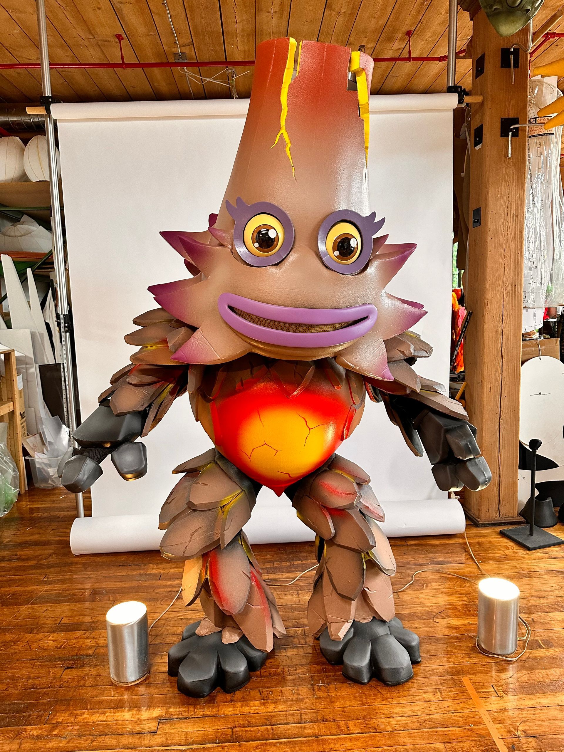A mascot is standing on a wooden floor in front of a white backdrop