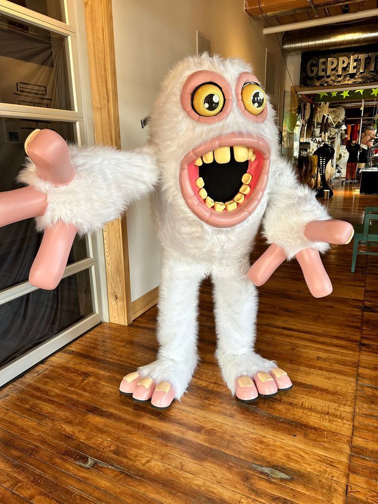 A white monster mascot is standing on a wooden floor in a room.