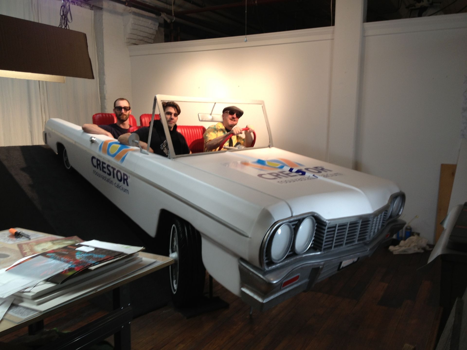 Three men are sitting in a white car that says crestor