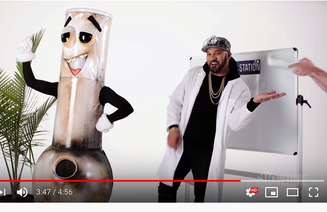 A man in a lab coat is standing next to a bong mascot.