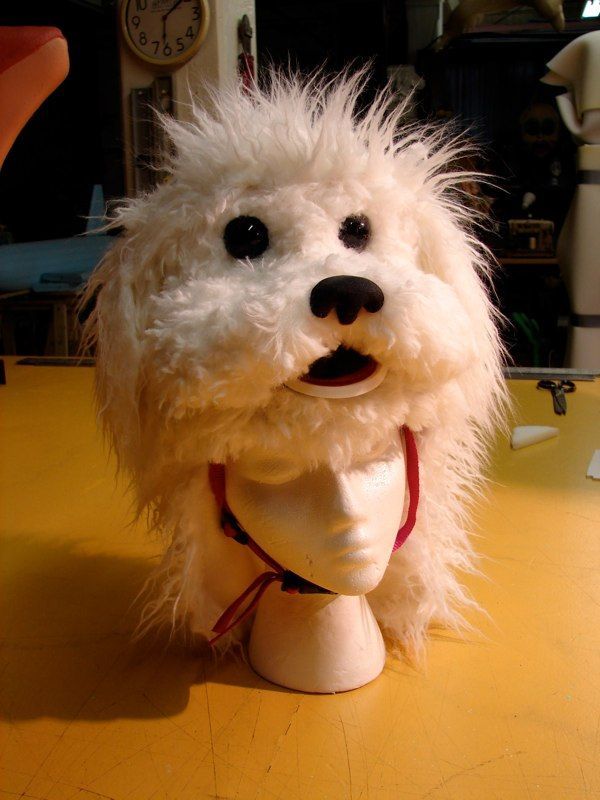 A stuffed dog is on a mannequin head on a table.