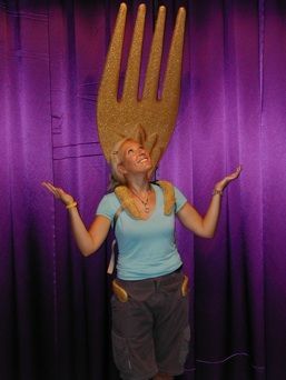 A woman is standing in front of a purple curtain with a large fork on her head.