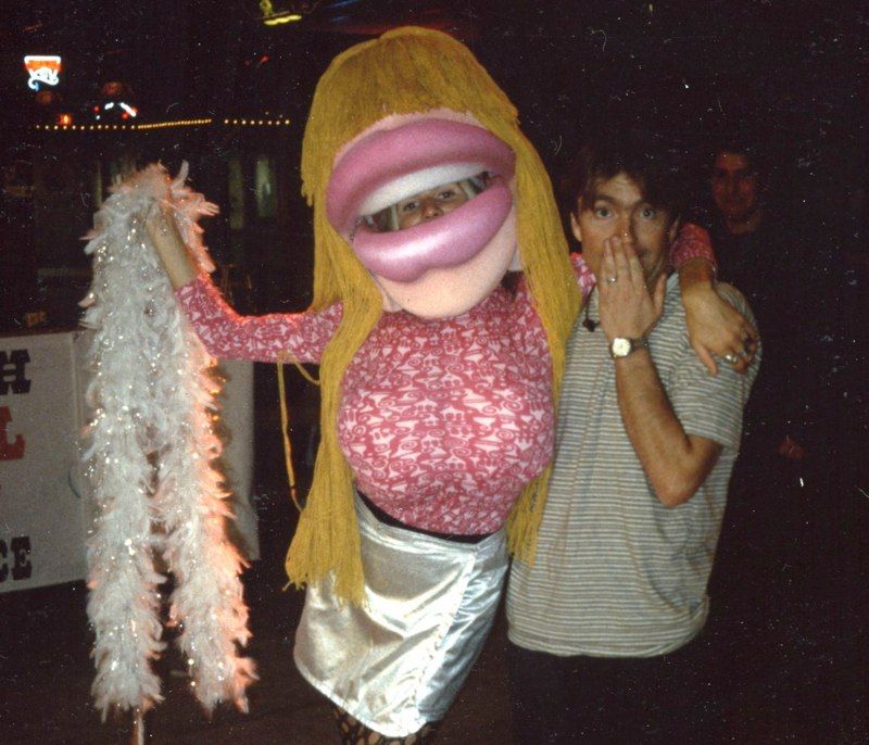 A man covering his mouth while standing next to a puppet