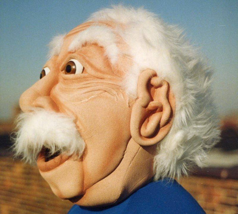 A puppet with a beard and white hair is wearing a blue shirt