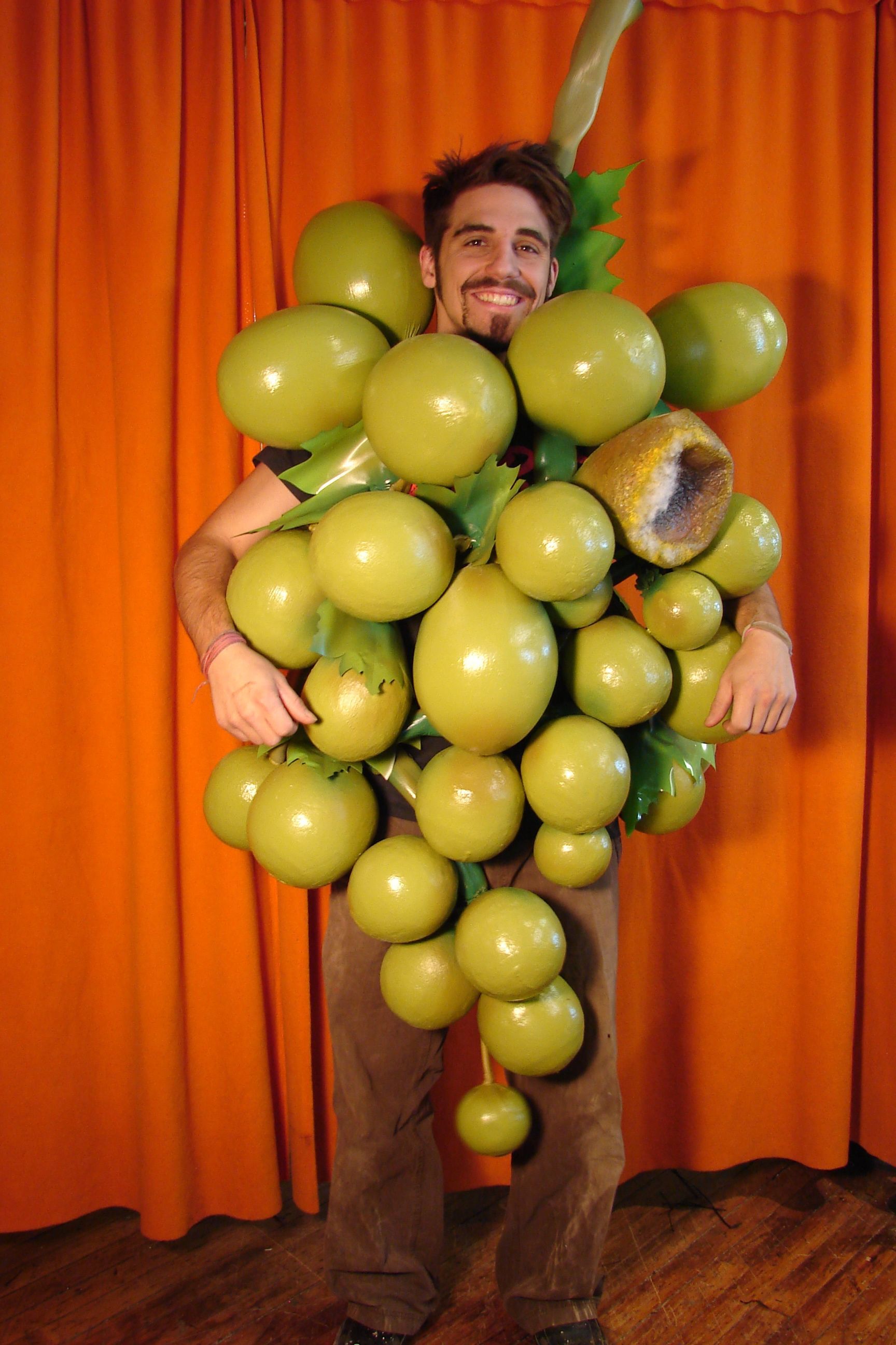 A man in a grape costume is standing in front of an orange curtain
