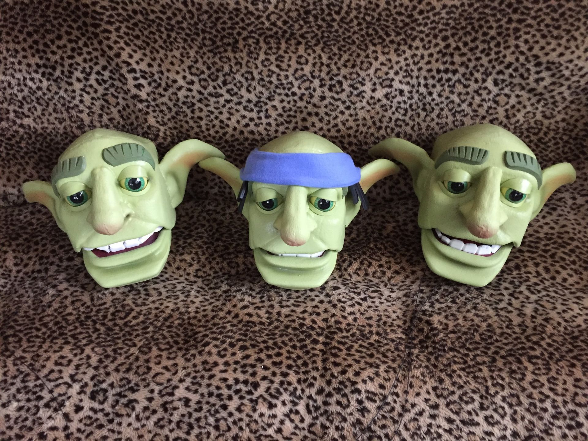 Three green goblin heads are sitting on a leopard print cloth