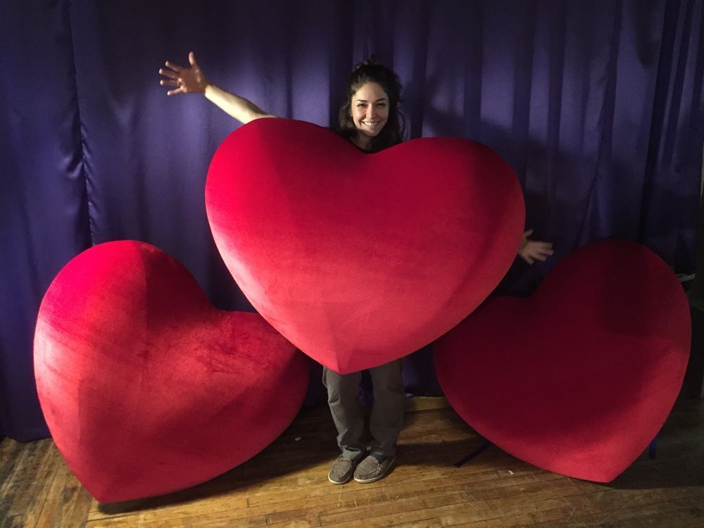A woman is standing next to three giant red hearts.