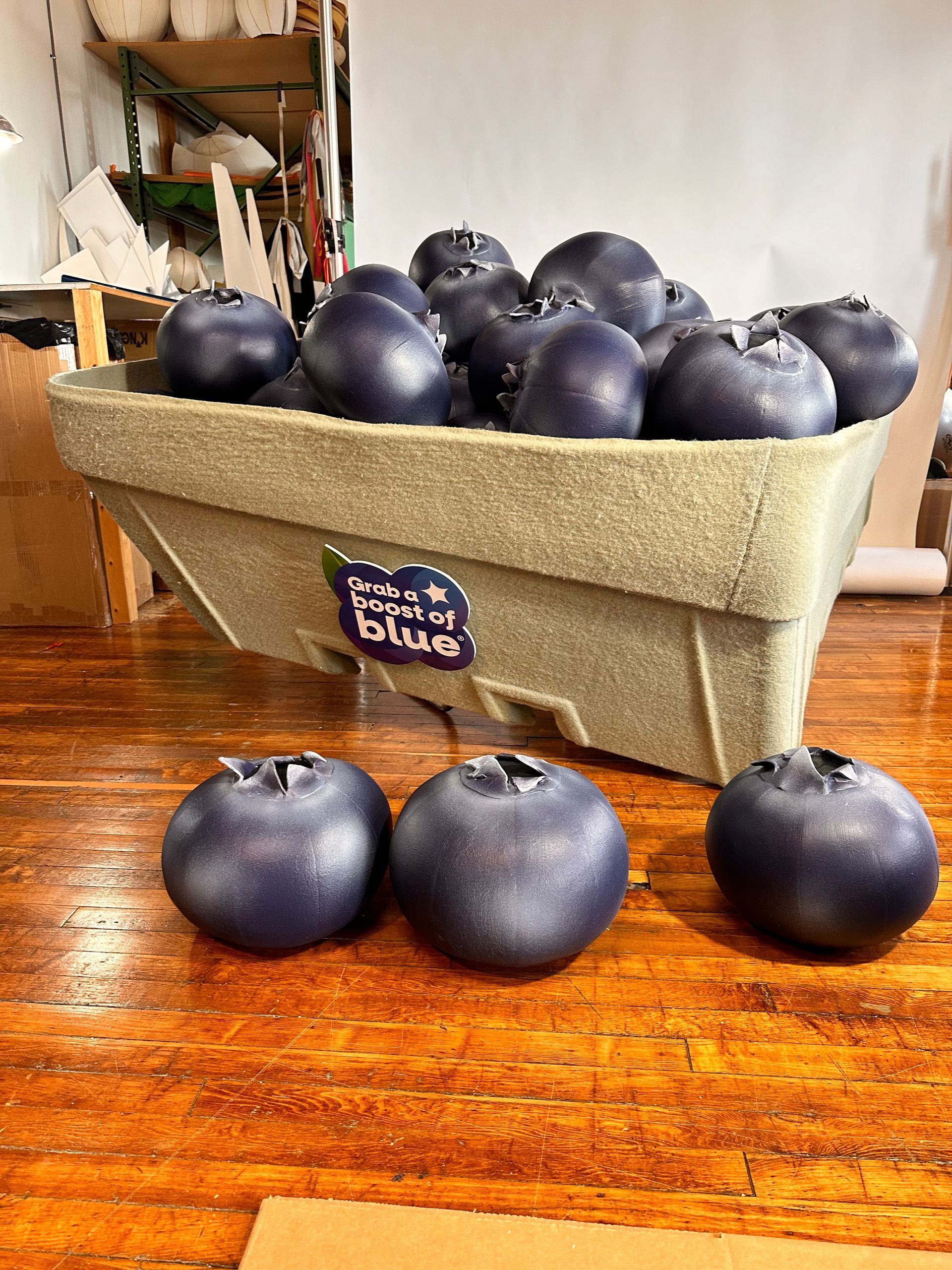 A box overflowing with large, deep blue blueberries on a wooden table, with three blueberries in front.