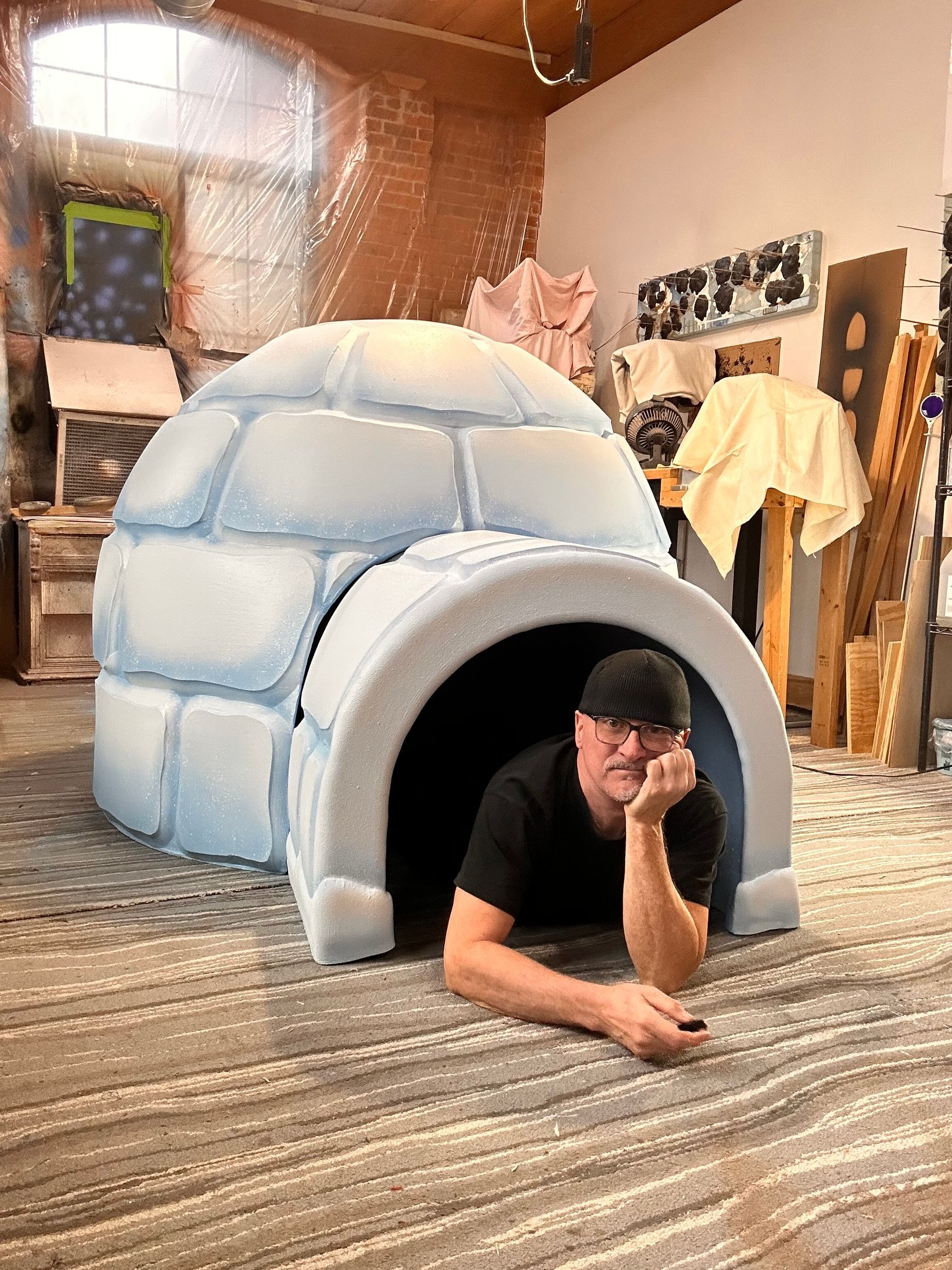 Man leaning in a painted igloo, inside a studio space.