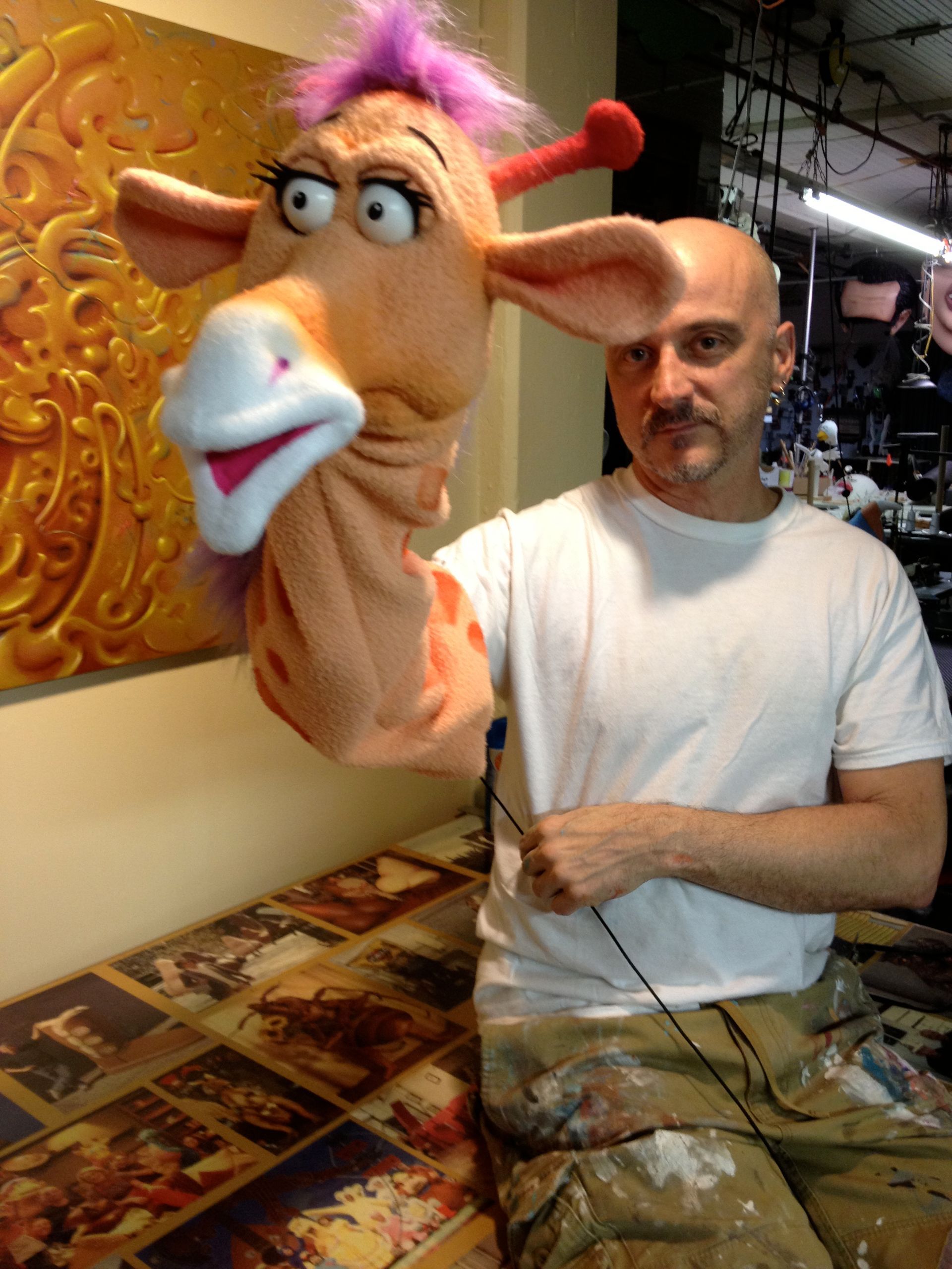 A man is holding a giraffe puppet with purple hair