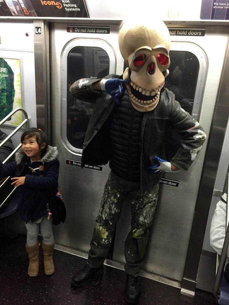 A man in a skeleton costume is standing next to a little girl on a train.