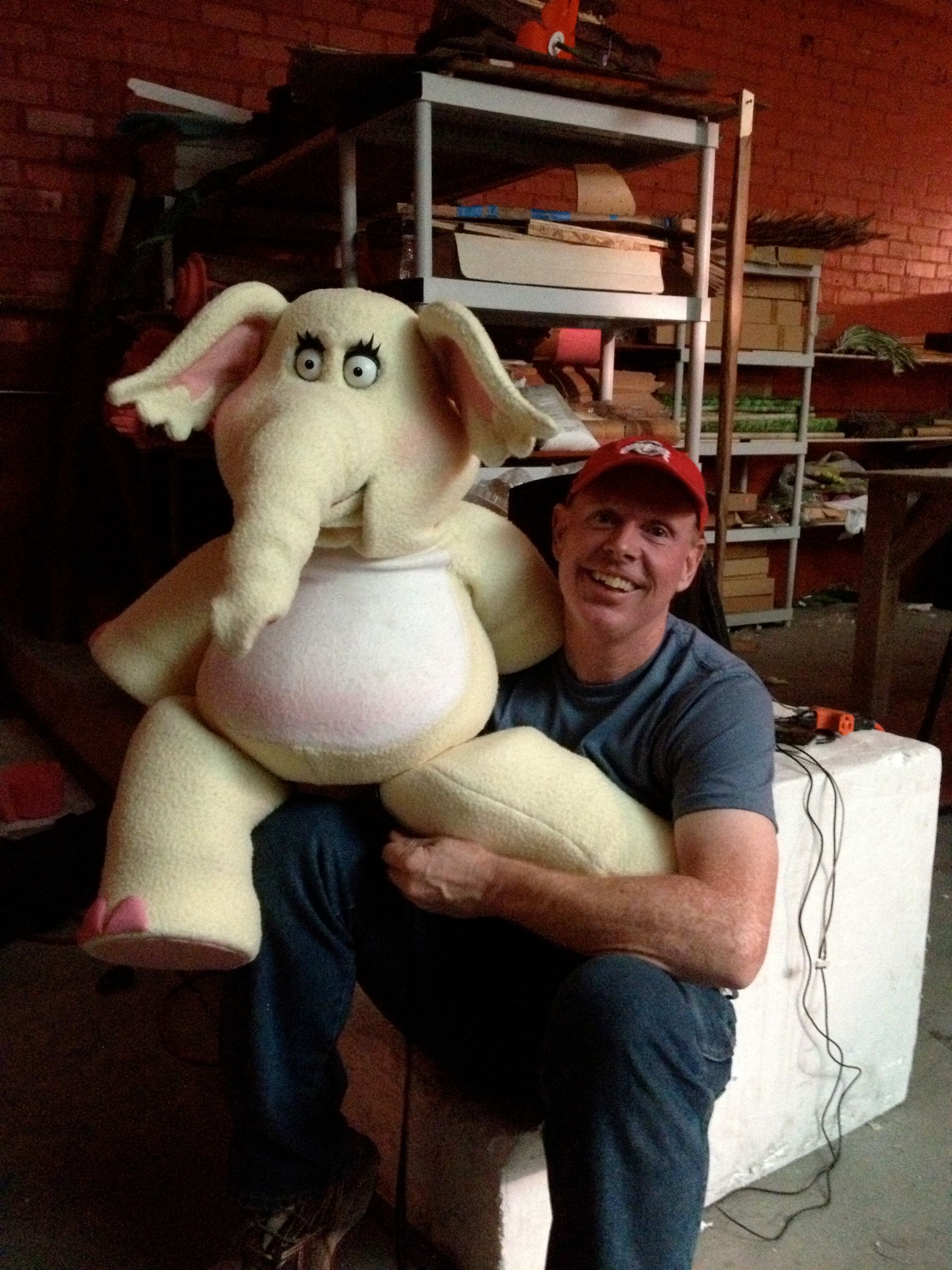 A man sitting next to a stuffed elephant wearing a red hat