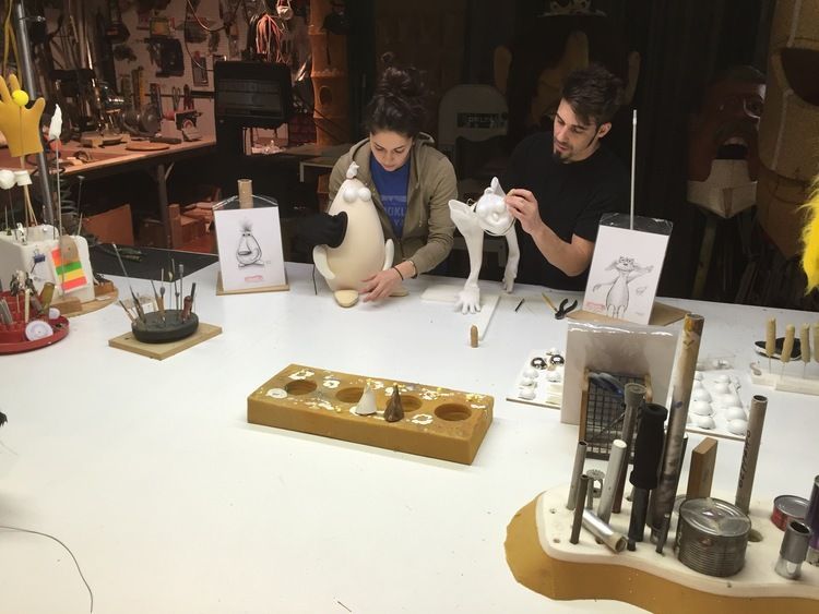 A man and a woman are sitting at a table working on a sculpture.