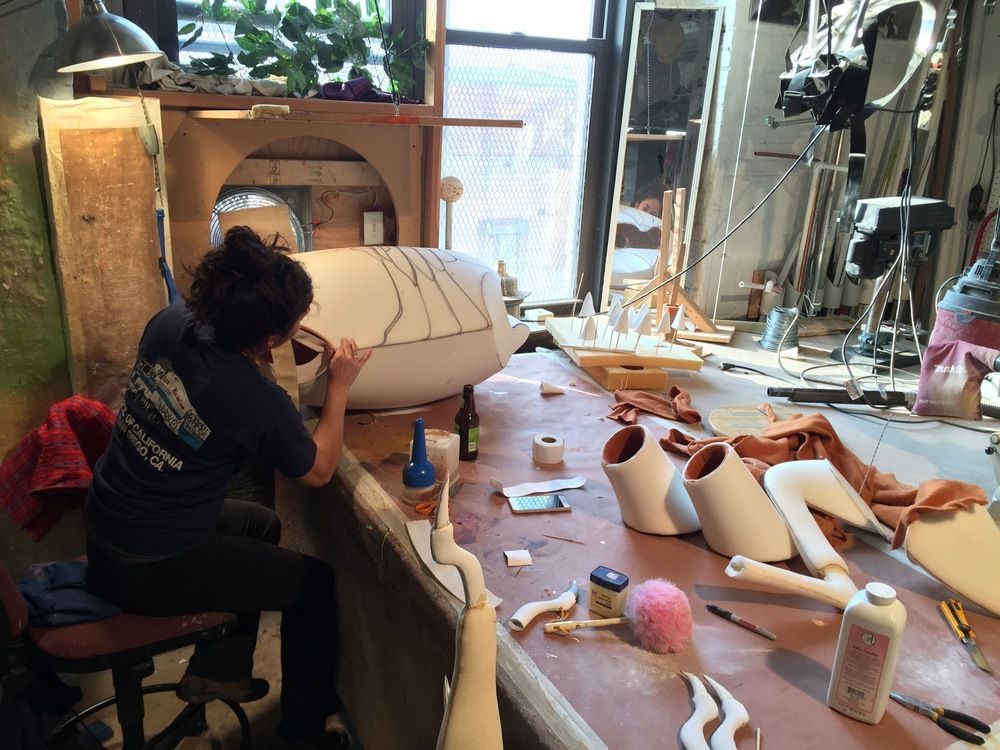 A woman is sitting at a table working on a sculpture
