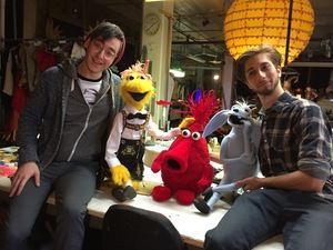 Two men are sitting next to stuffed animals on a table.