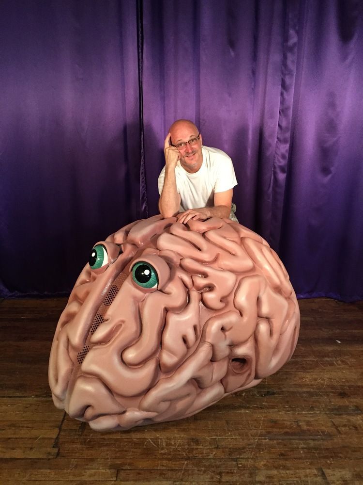 A man is sitting on top of a giant brain with green eyes.