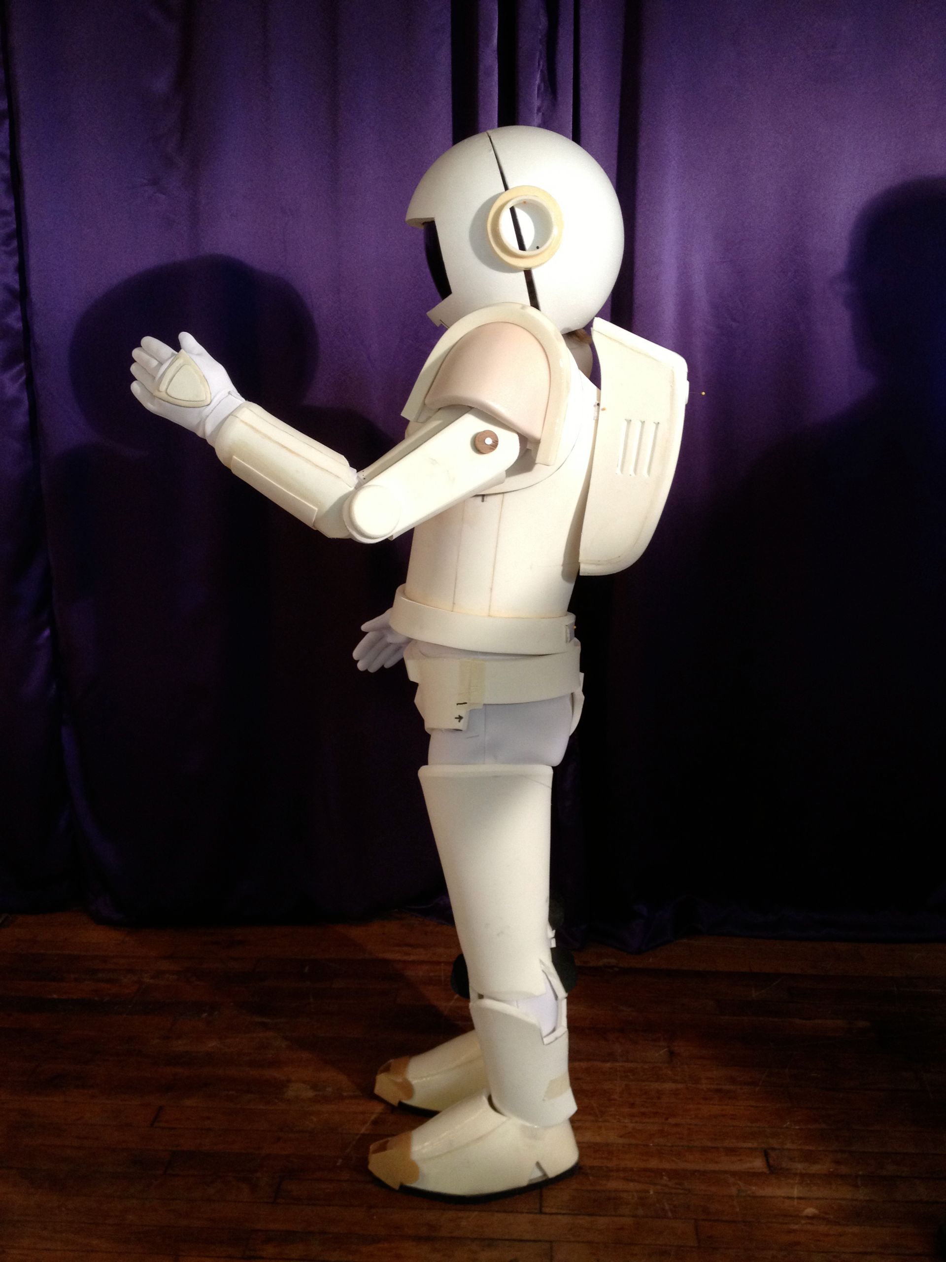 A white robot is standing in front of a purple curtain