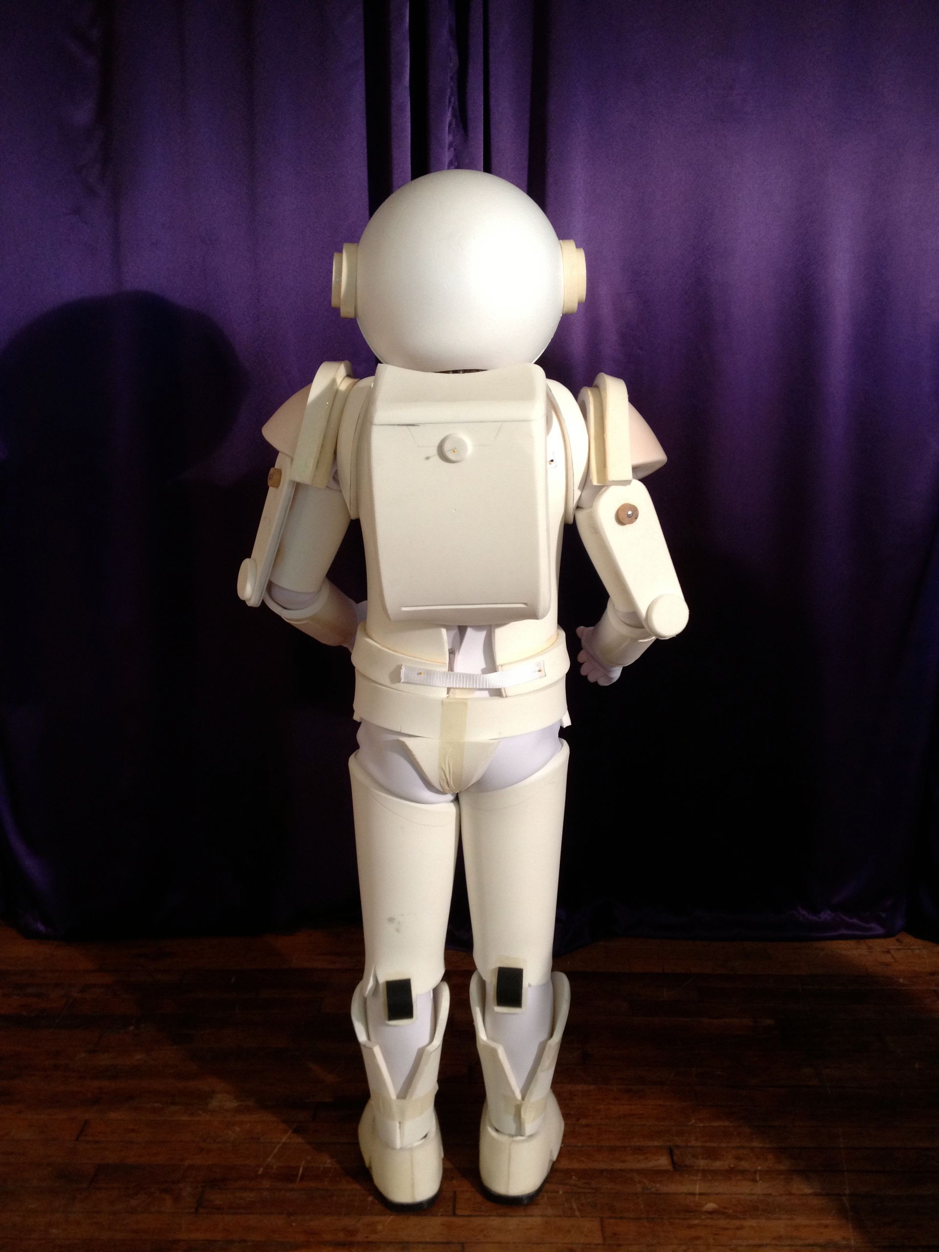 A white robot is standing in front of a purple curtain
