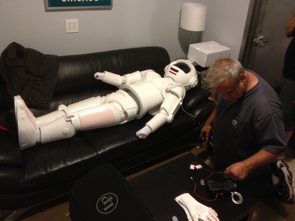A man is working on a robot that is laying on a couch