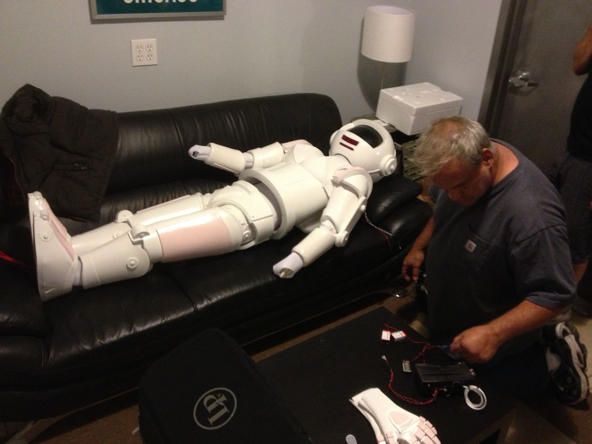 A man is working on a robot that is laying on a couch