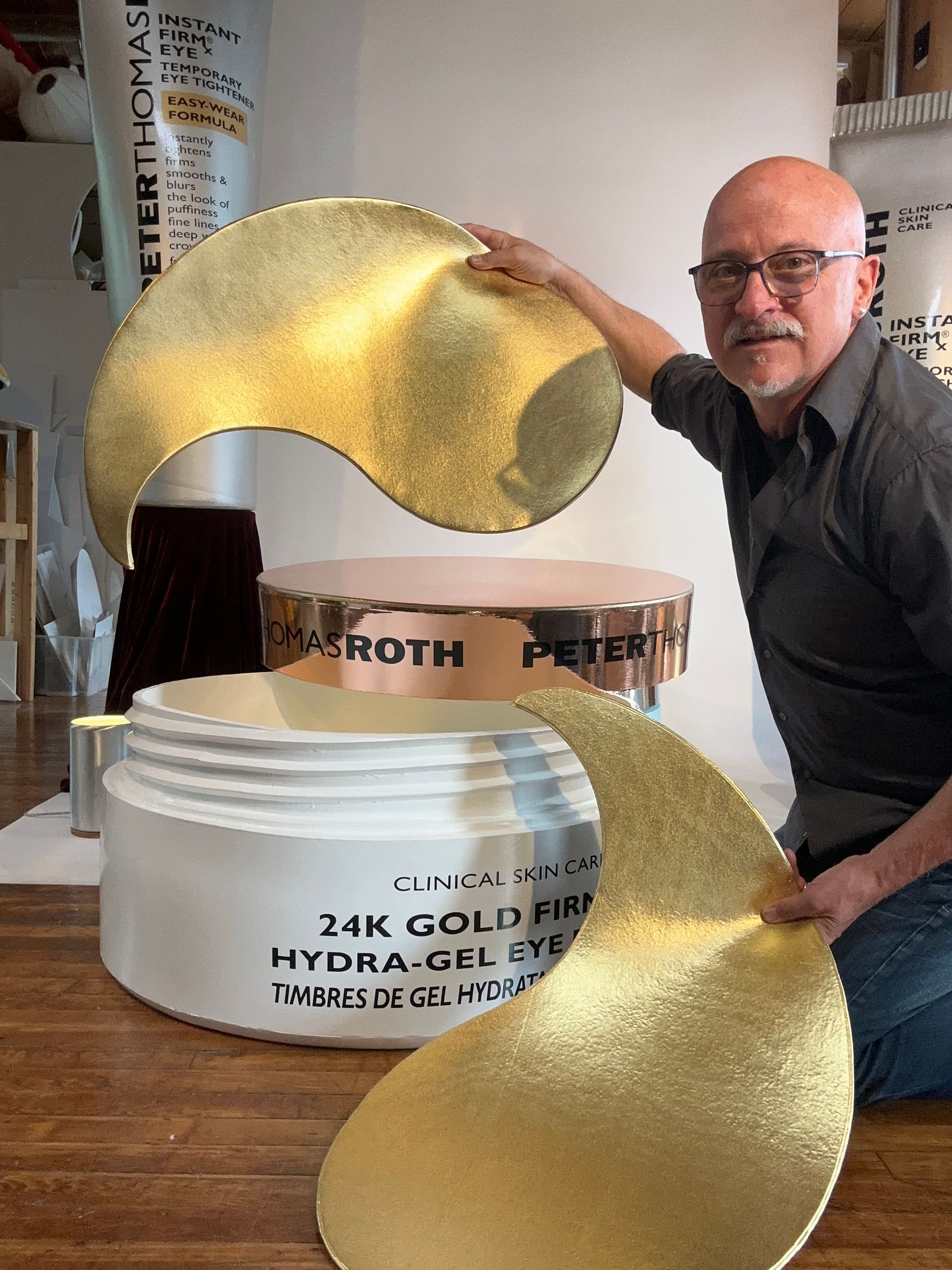 Man holding large golden eye patch next to a giant jar of Peter Thomas Roth eye gel.