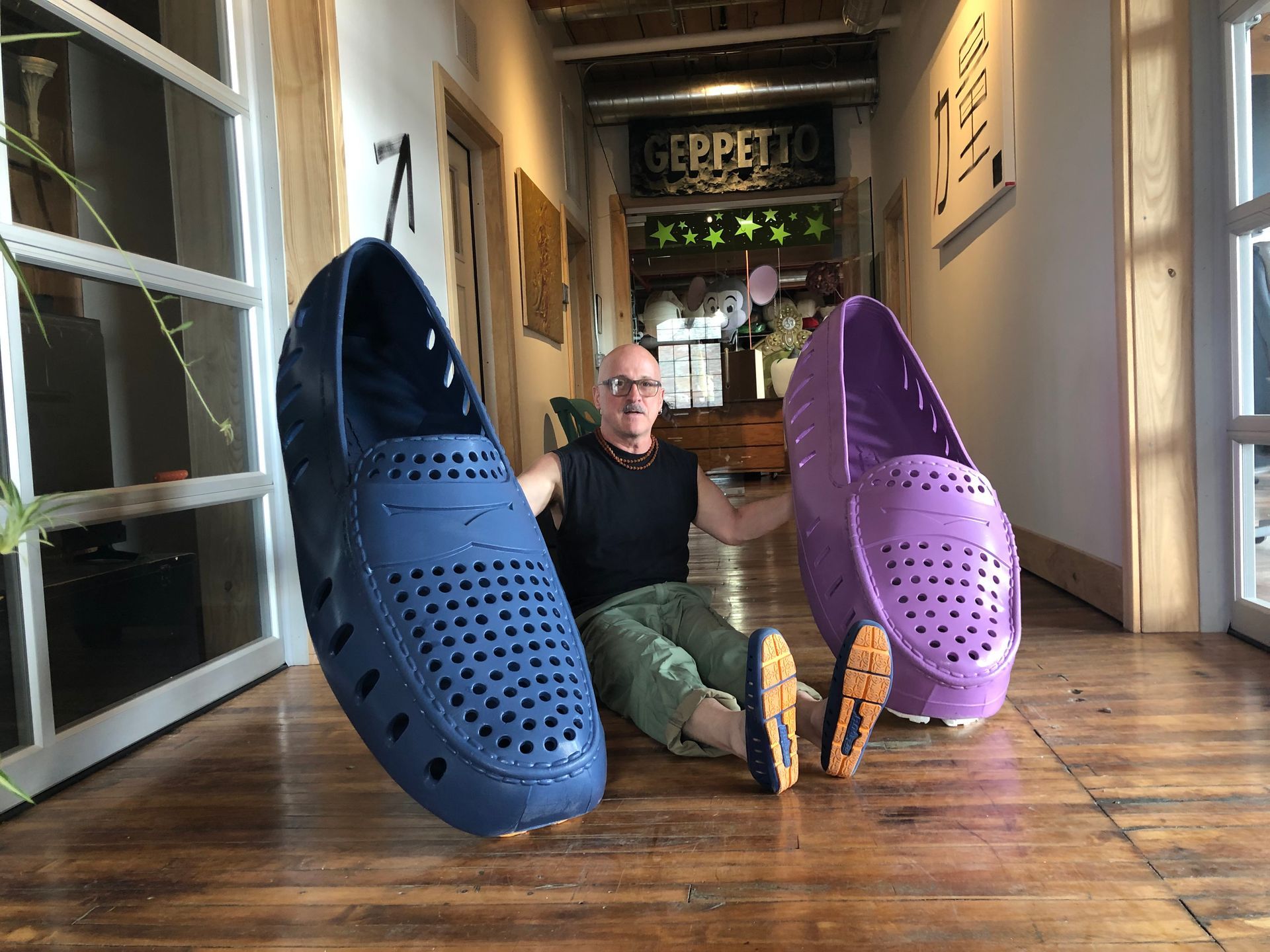 Man holding up large blue and purple shoes indoors.