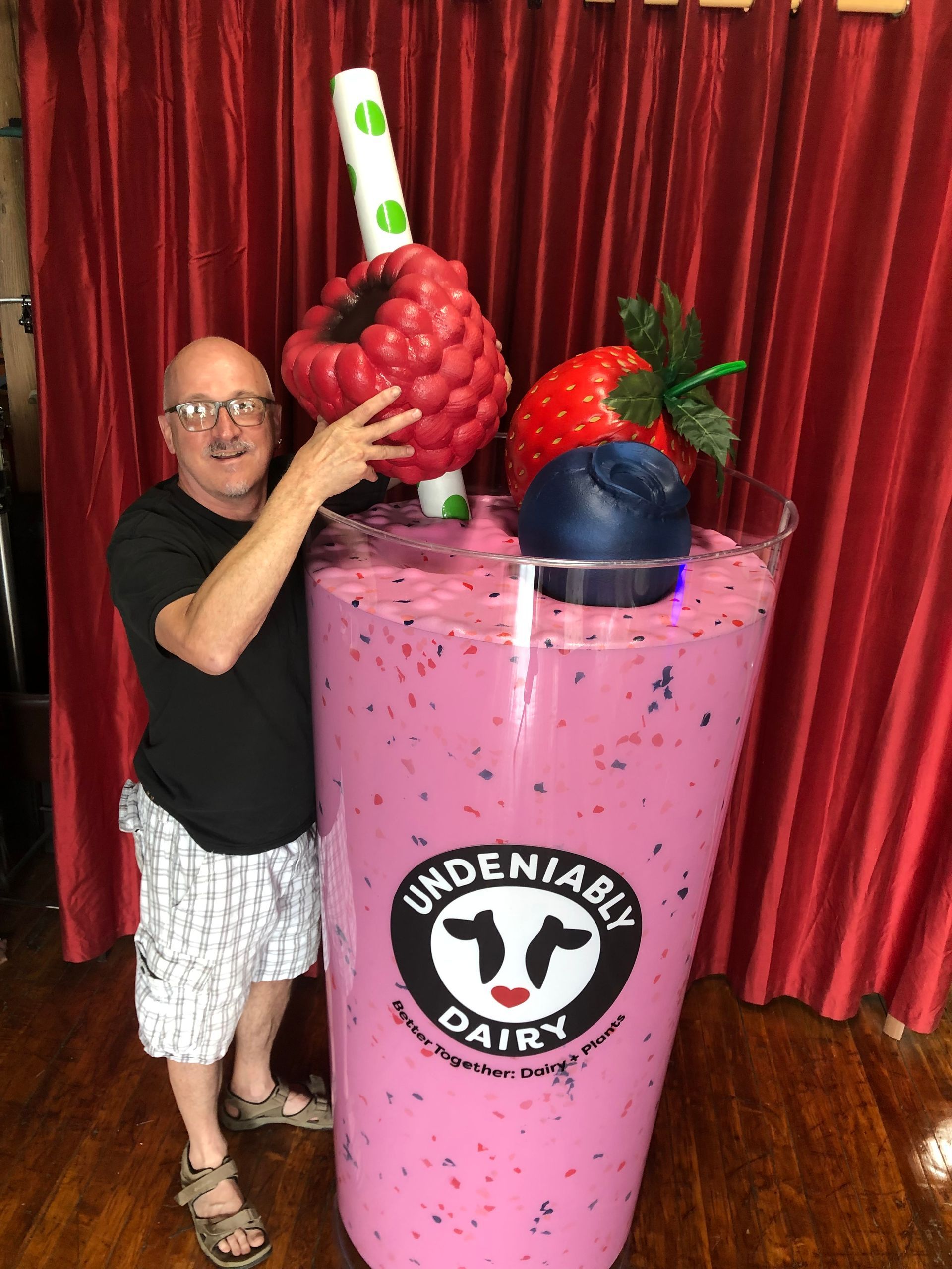 Man beside giant pink Undeniably Dairy milkshake with berry toppings.