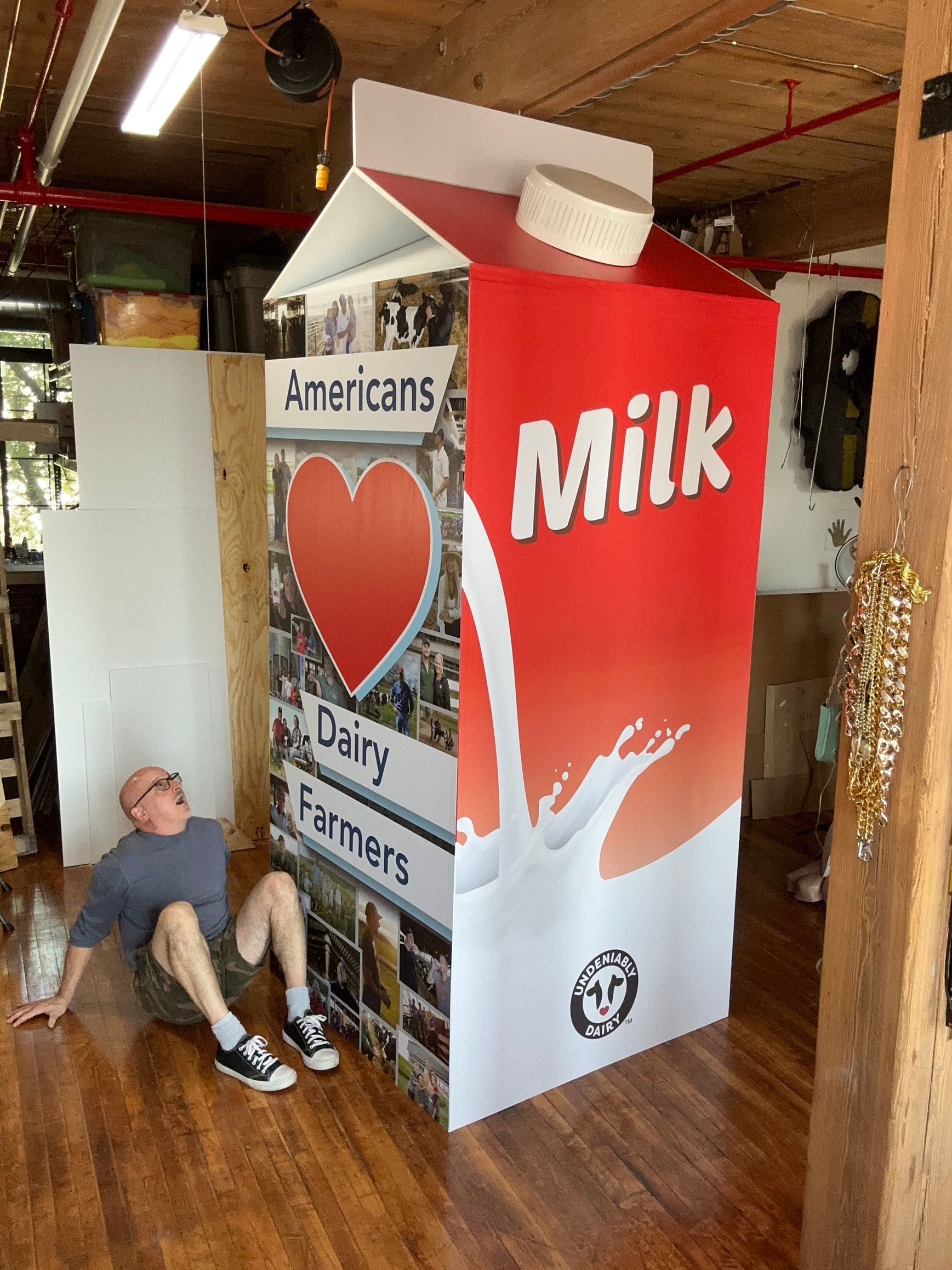 Man beside a giant milk carton prop; he looks up, mouth open. Carton is red, white, and has the word 