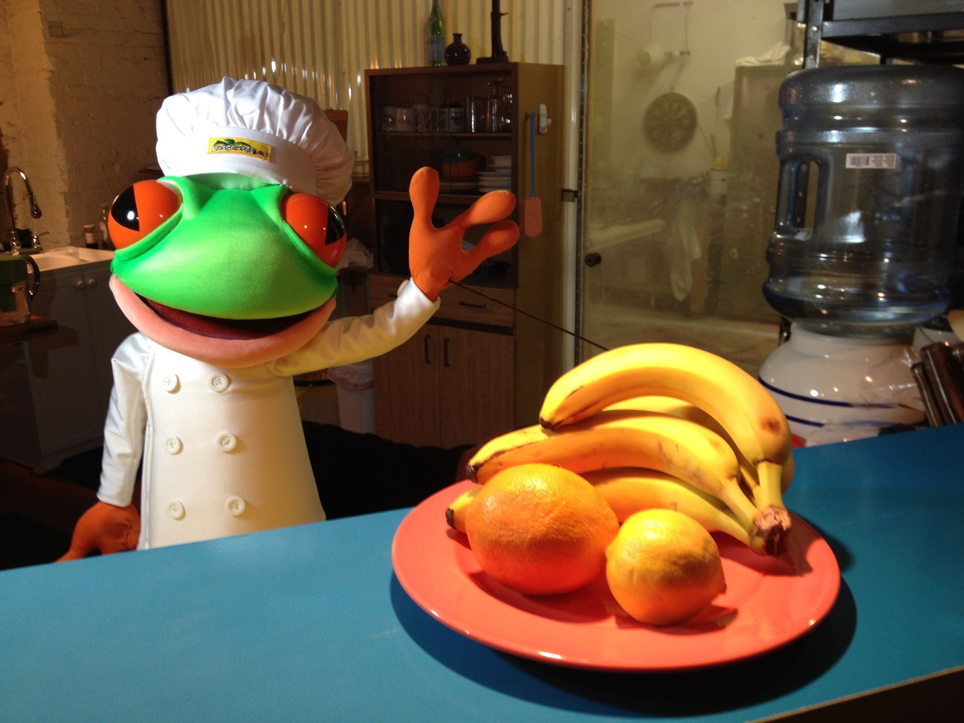 A frog mascot is standing next to a plate of fruit
