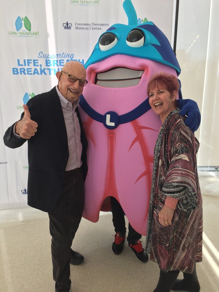 A man and woman standing next to a mascot that has the letter l on it