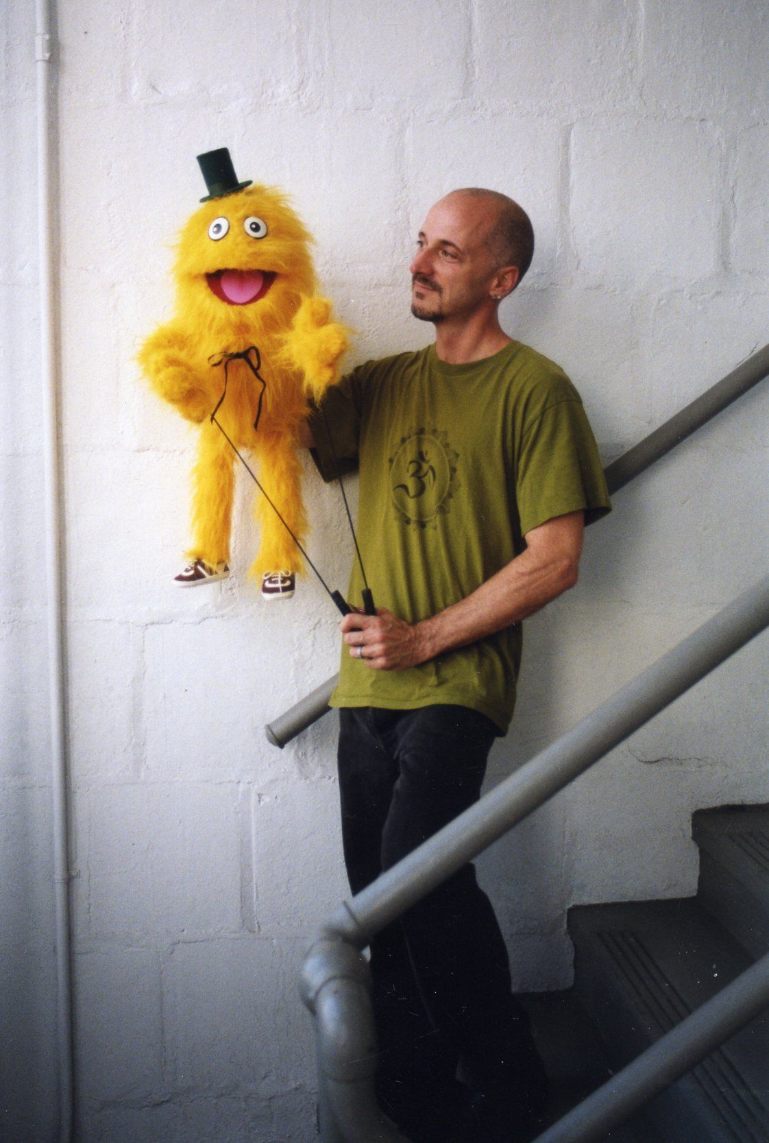 A man is holding a yellow puppet with a top hat on it