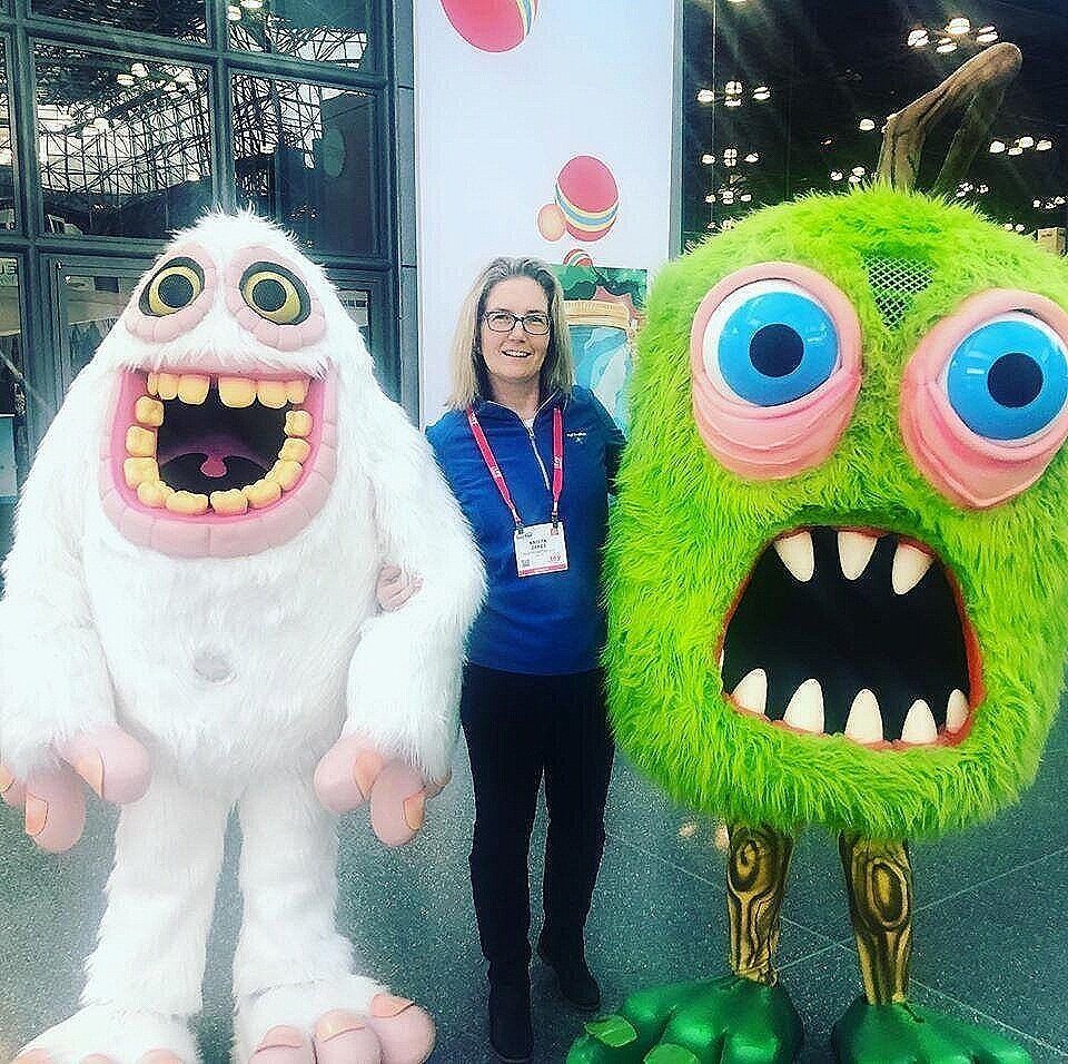 A woman is standing next to a green monster and a white monster