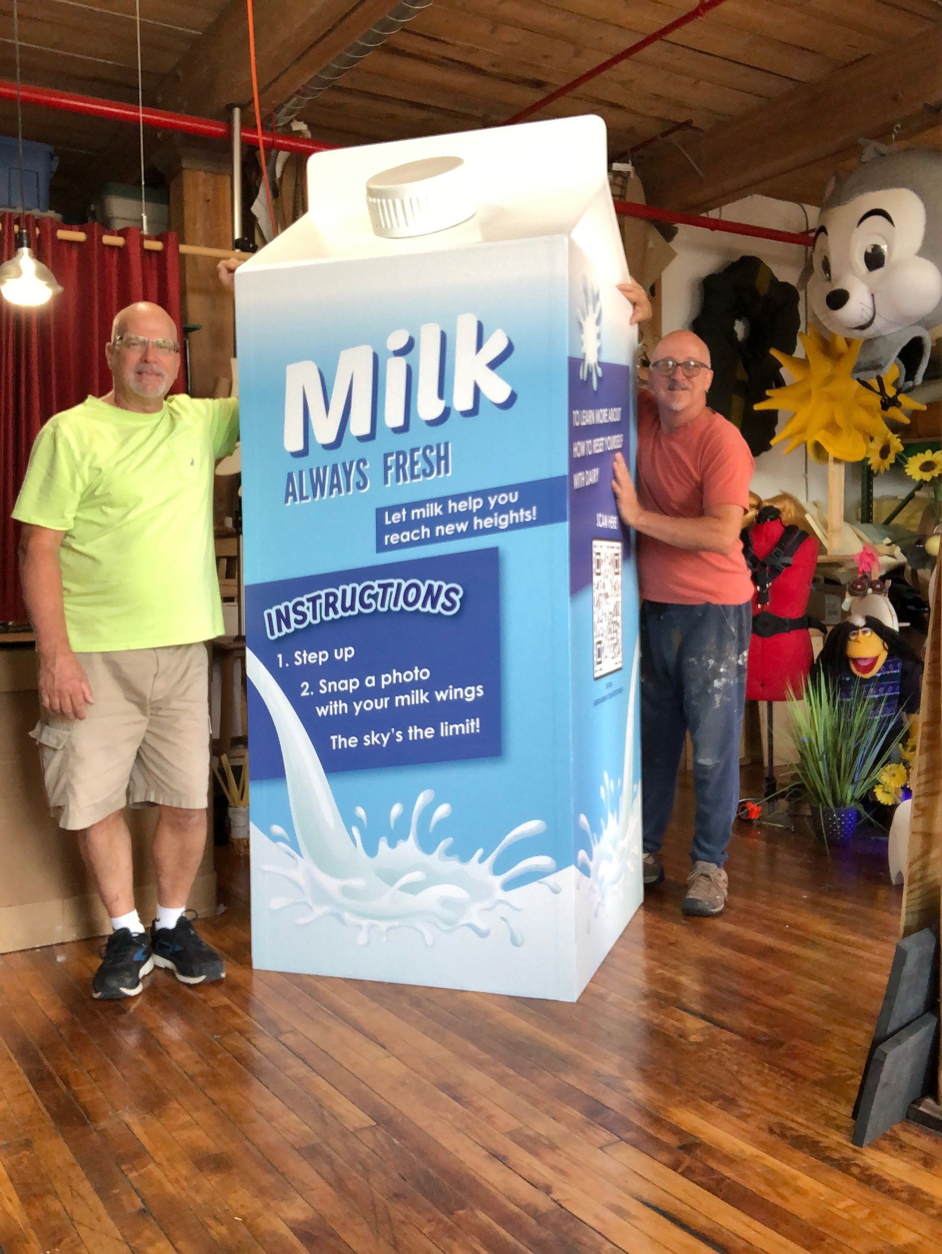Two men standing next to a large carton of milk