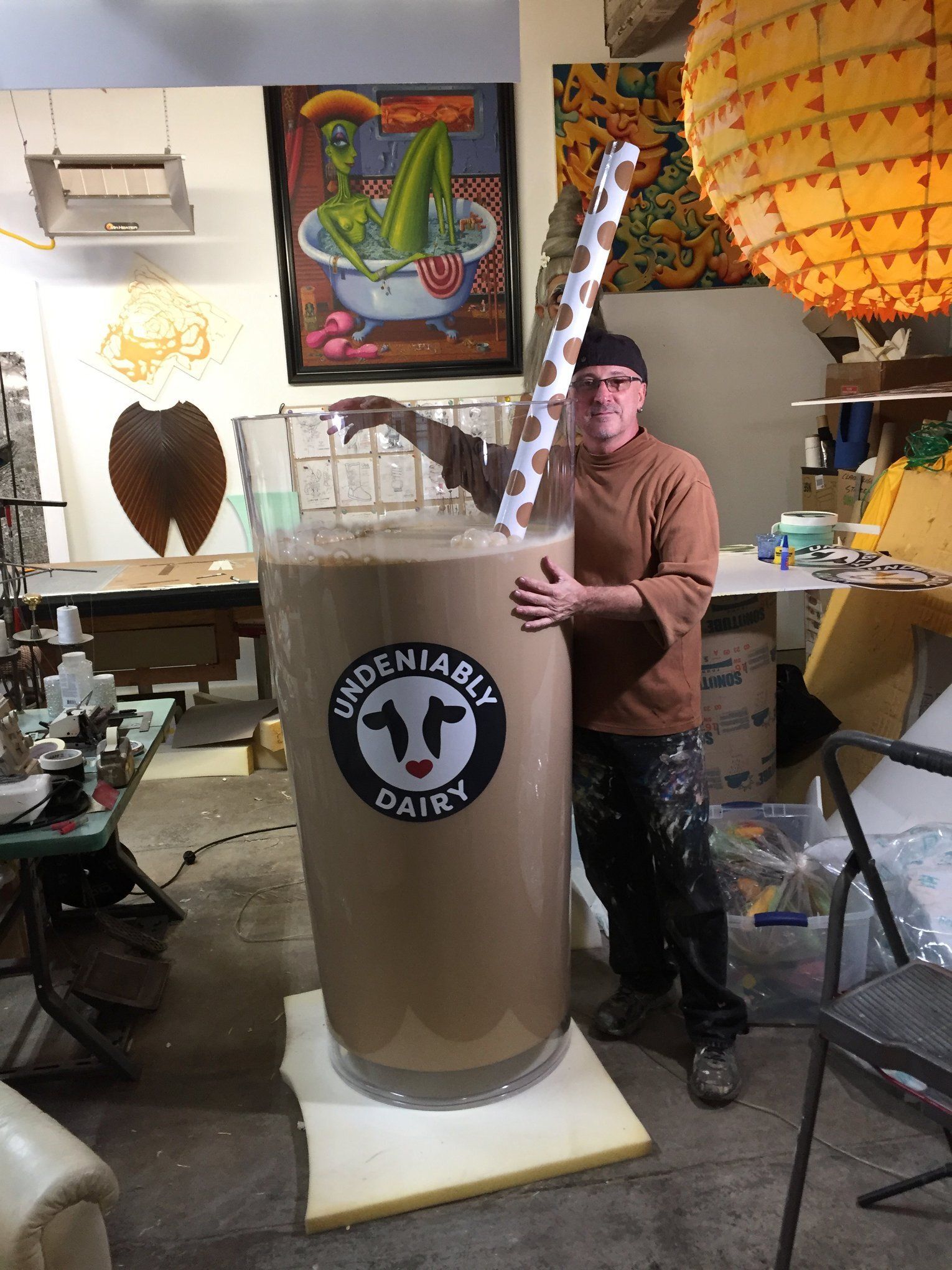 A man is holding a giant milkshake glass in a room.