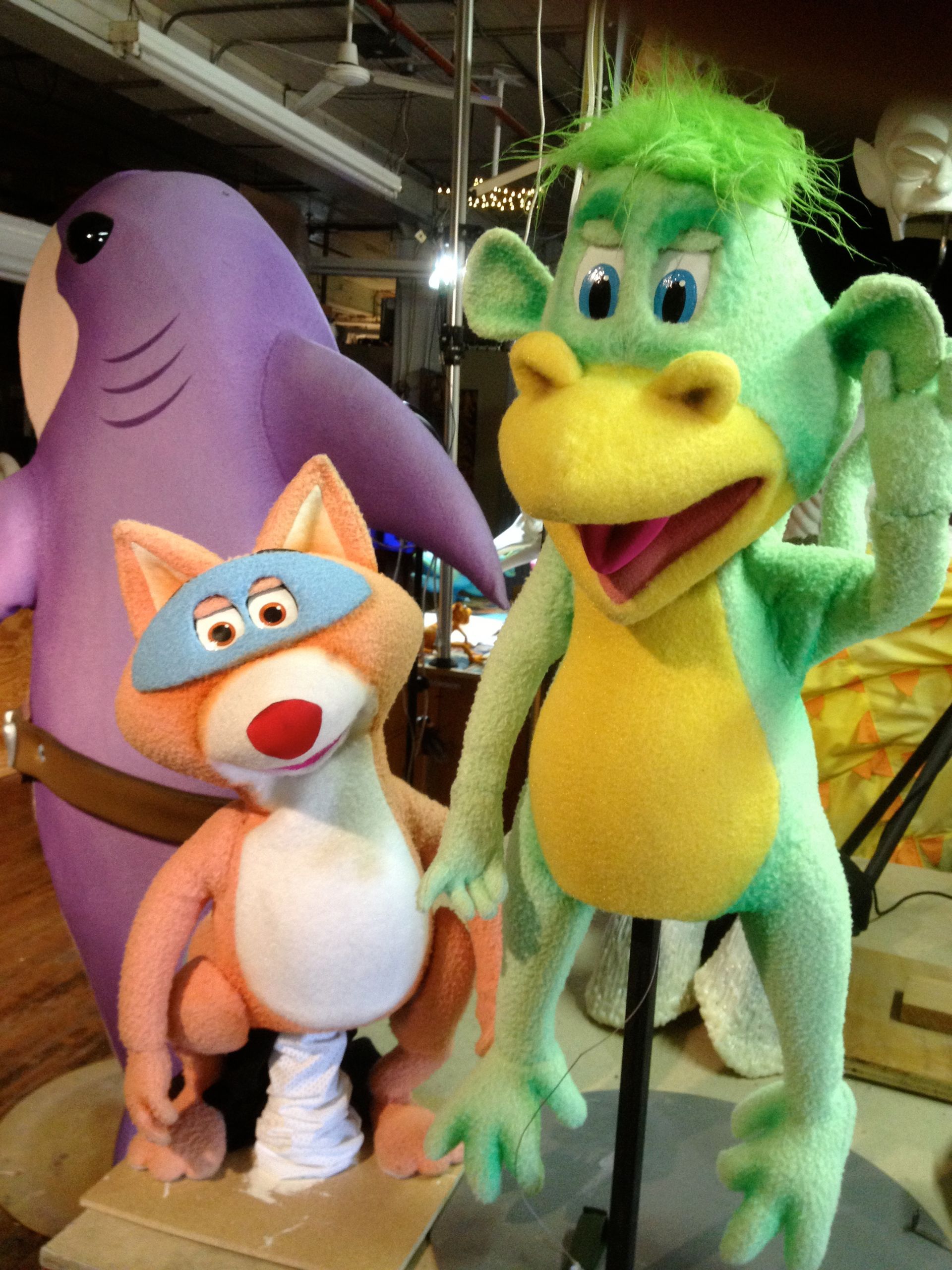 A purple shark a cat and a green frog are standing next to each other