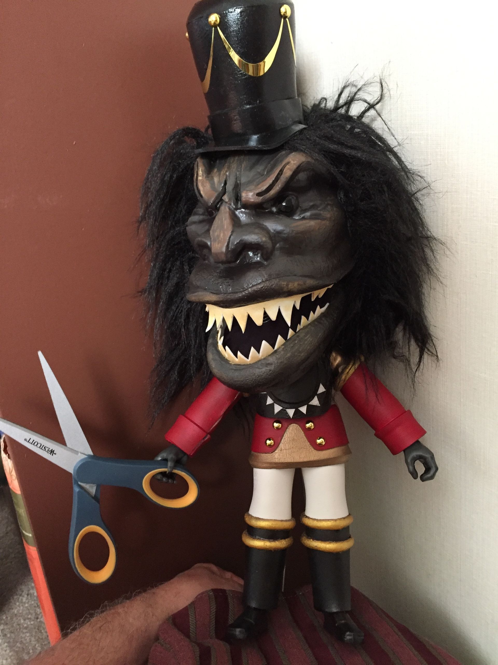 A toy with sharp teeth is holding a pair of scissors