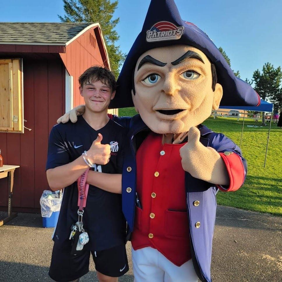 A boy standing next to a patriots mascot