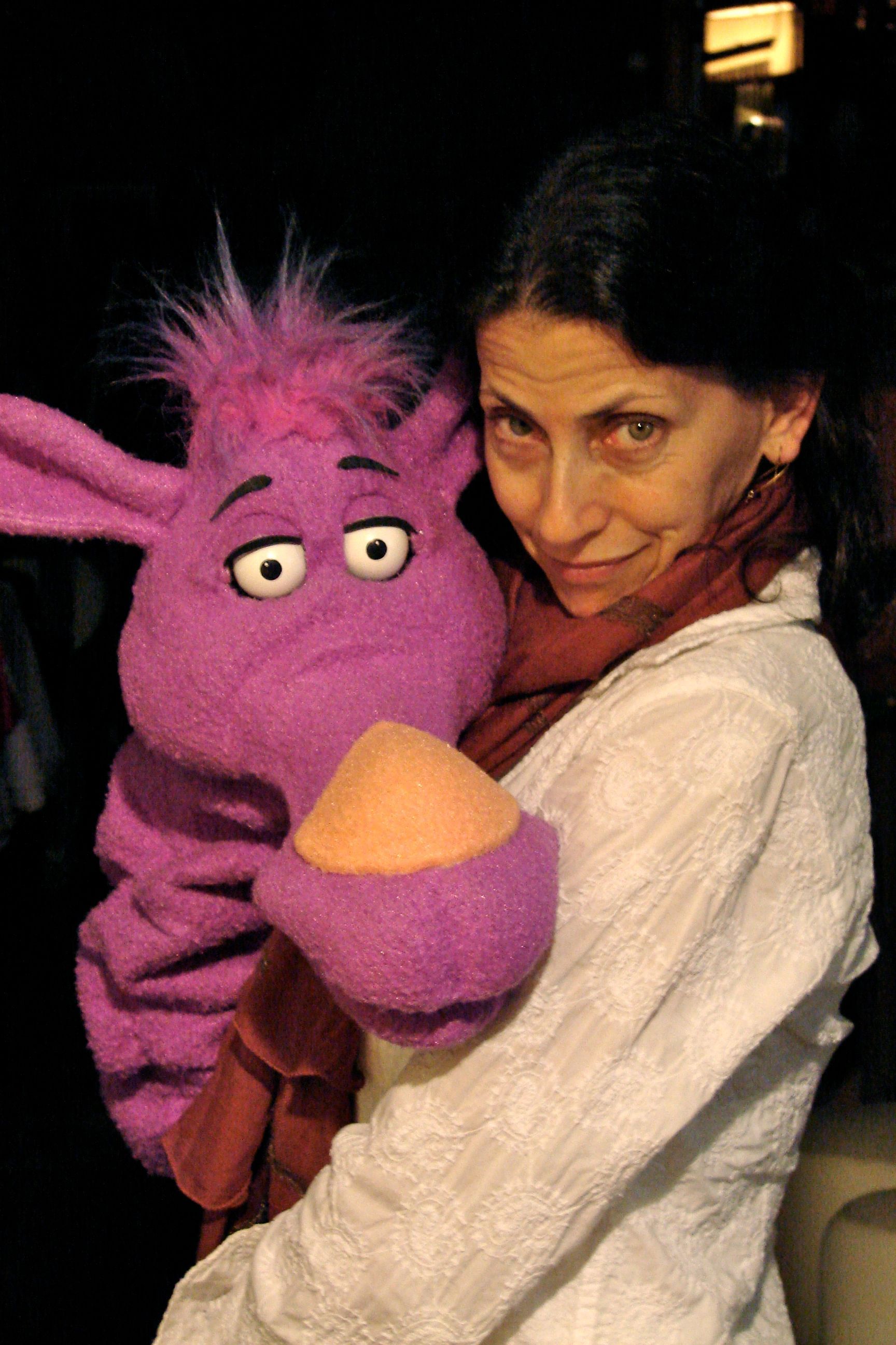 A woman is holding a purple puppet in her arms.