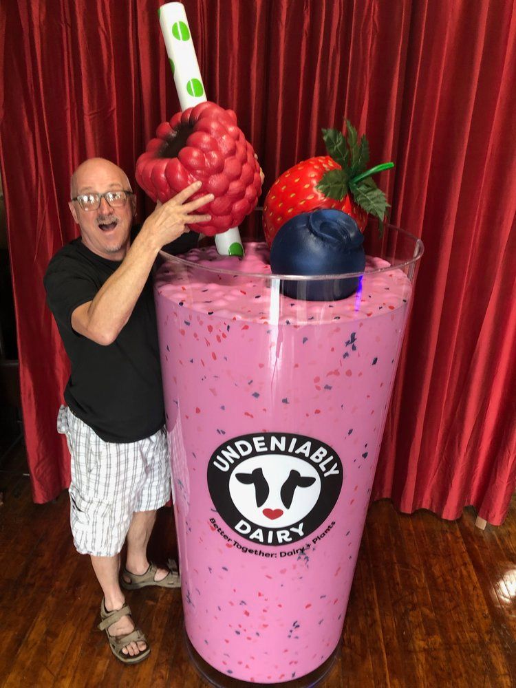 A man is standing next to a giant milkshake.