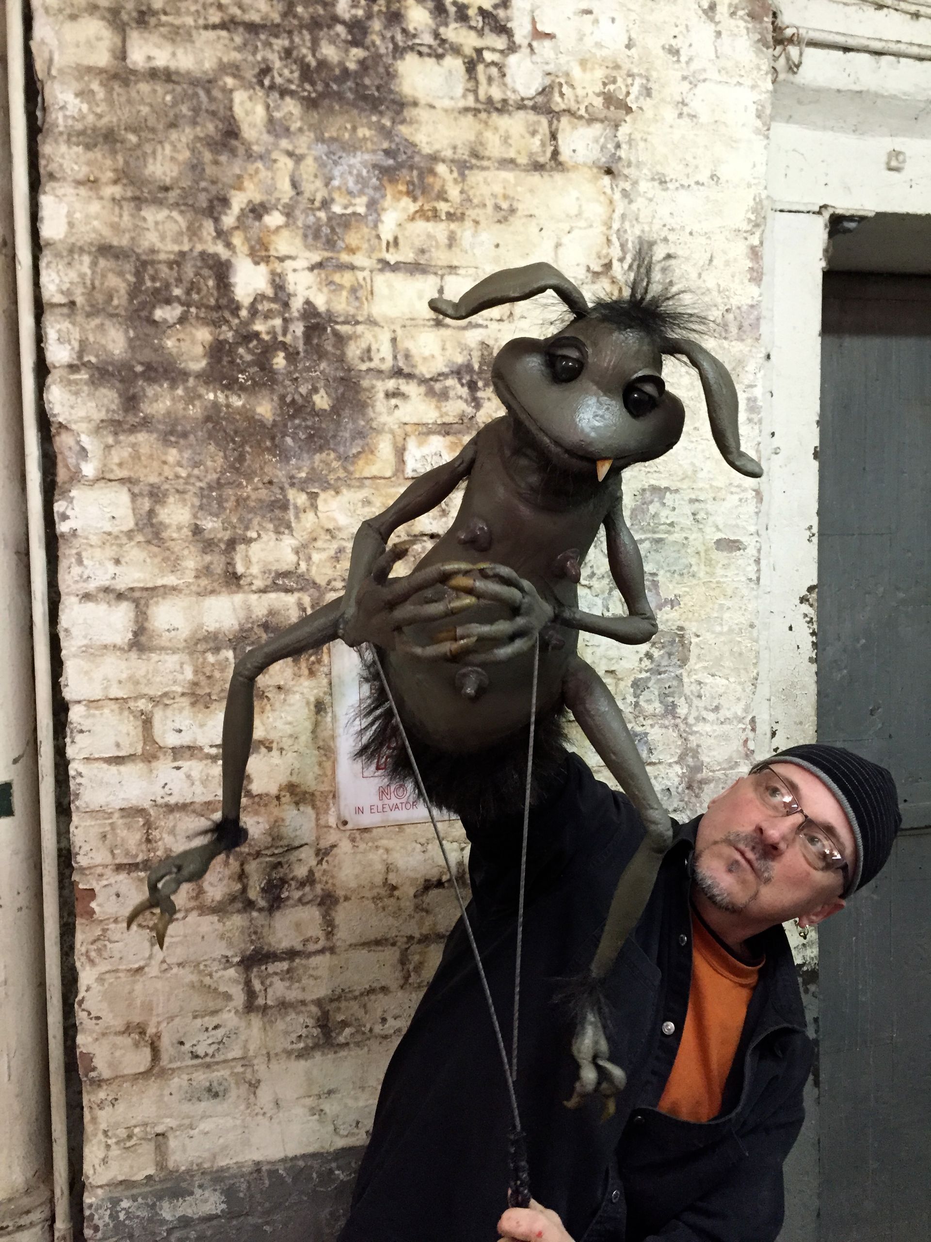 A man is holding a puppet in front of a brick wall