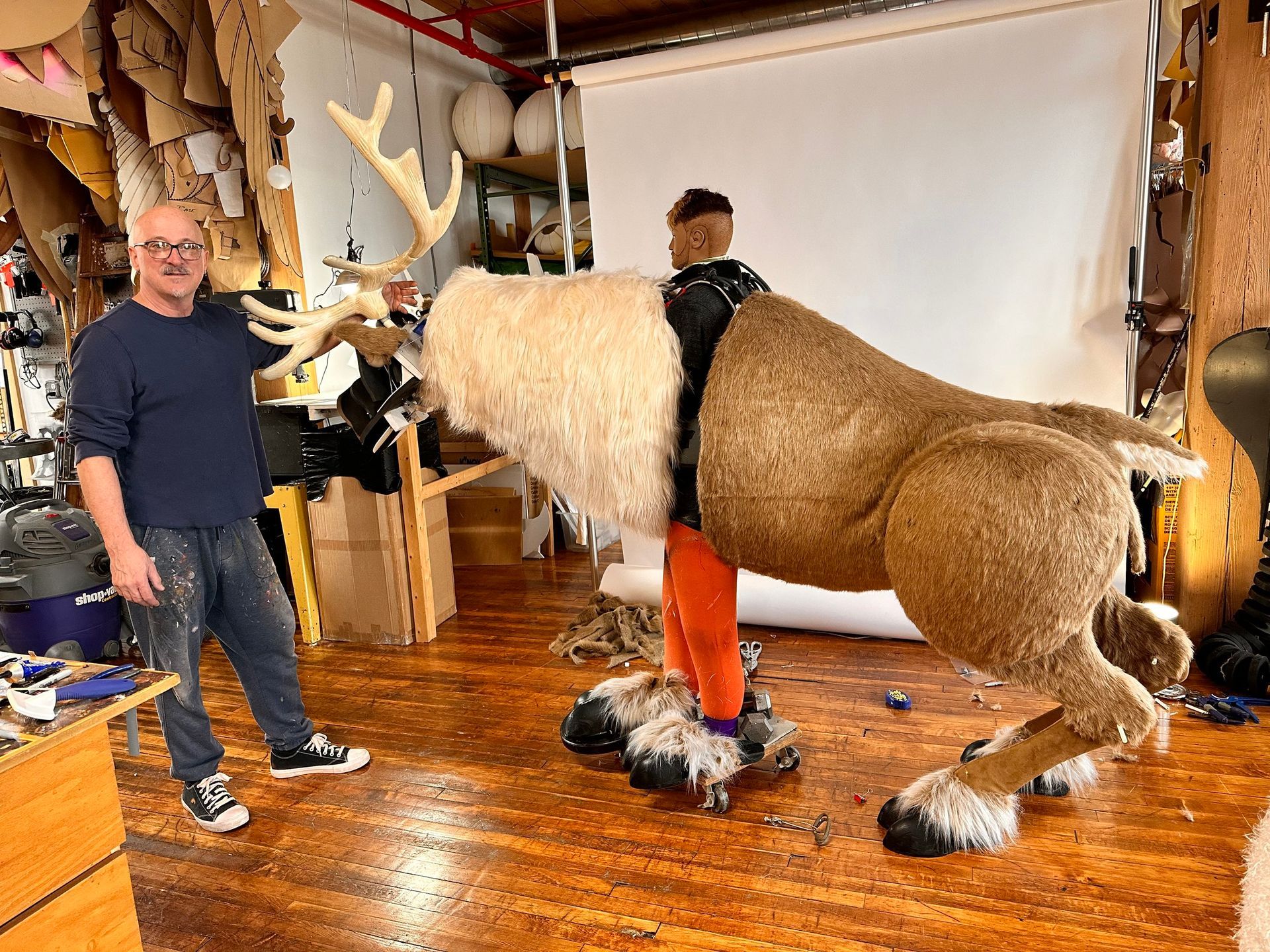 A man is standing next to a stuffed reindeer in a room.