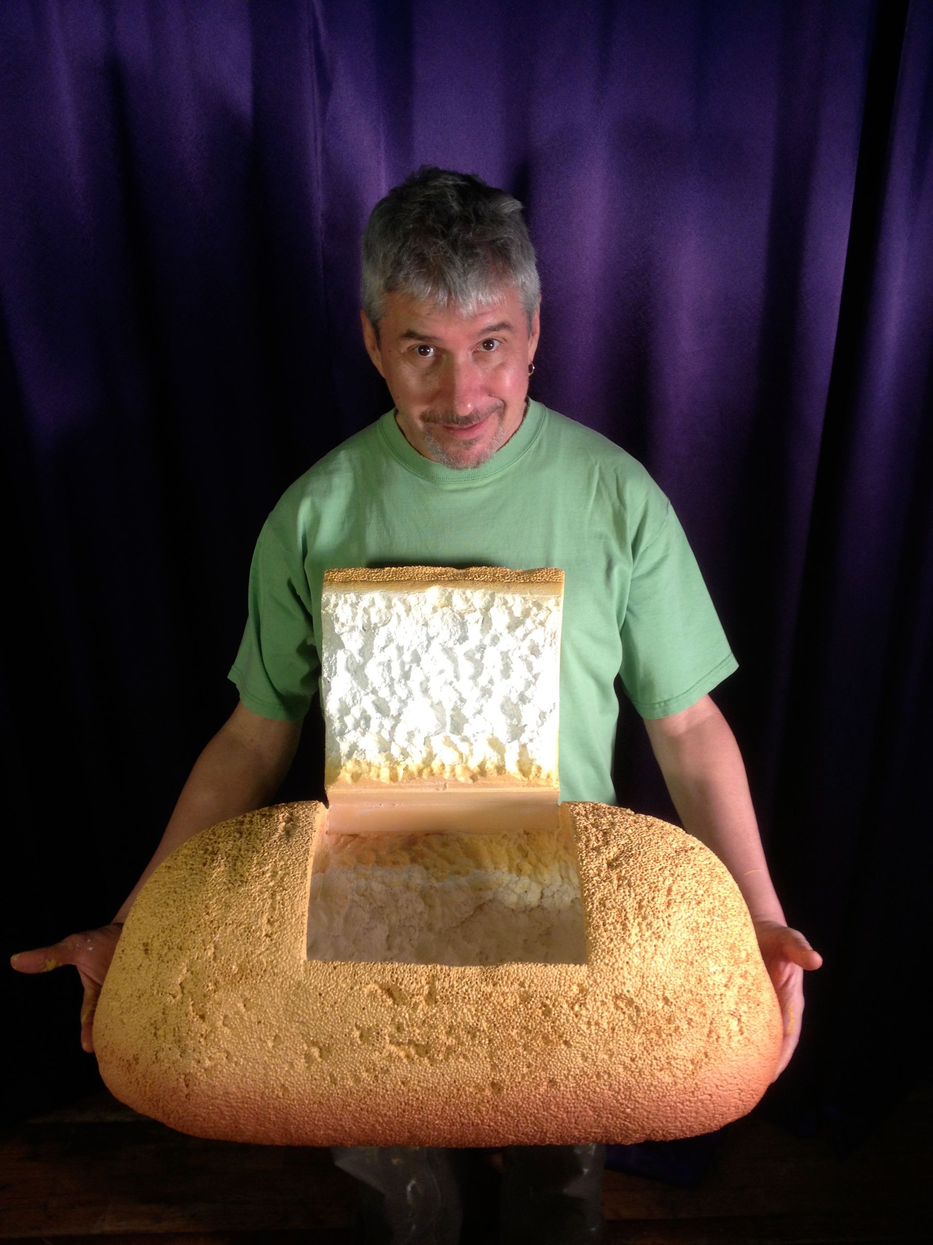 A man in a green shirt is holding a very large loaf of bread