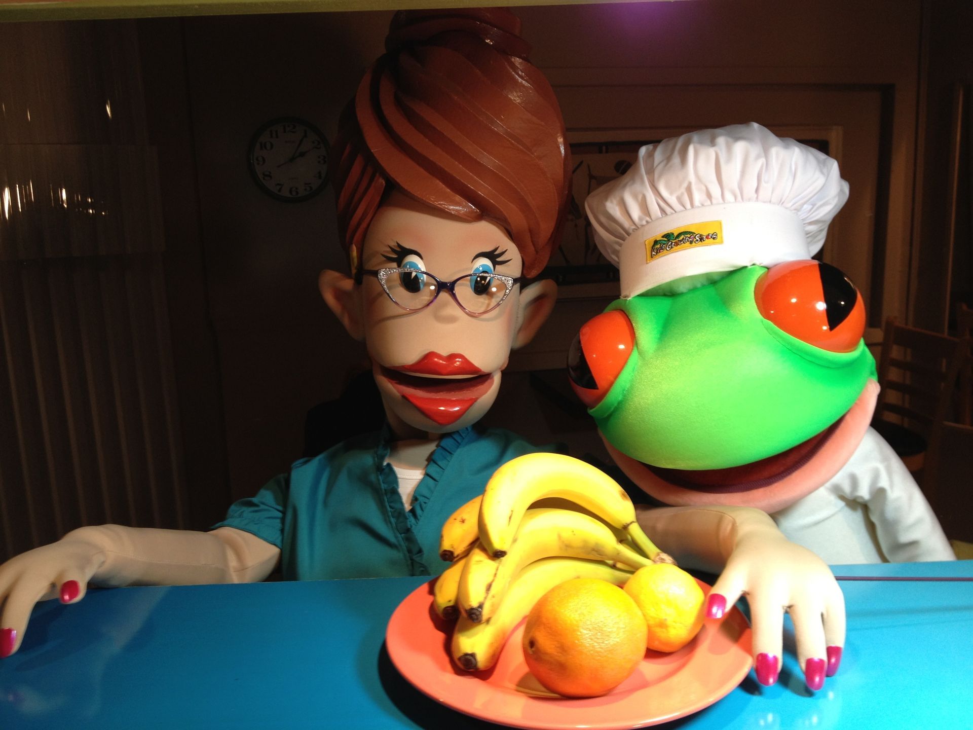 A frog and a woman are standing next to a plate of fruit