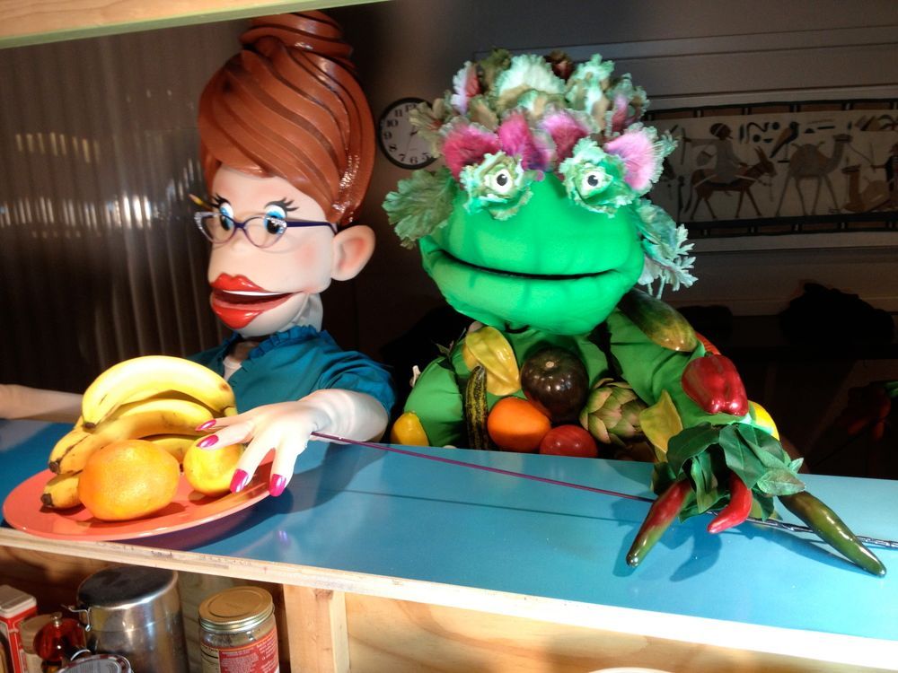 A woman holding a plate of bananas next to a green puppet
