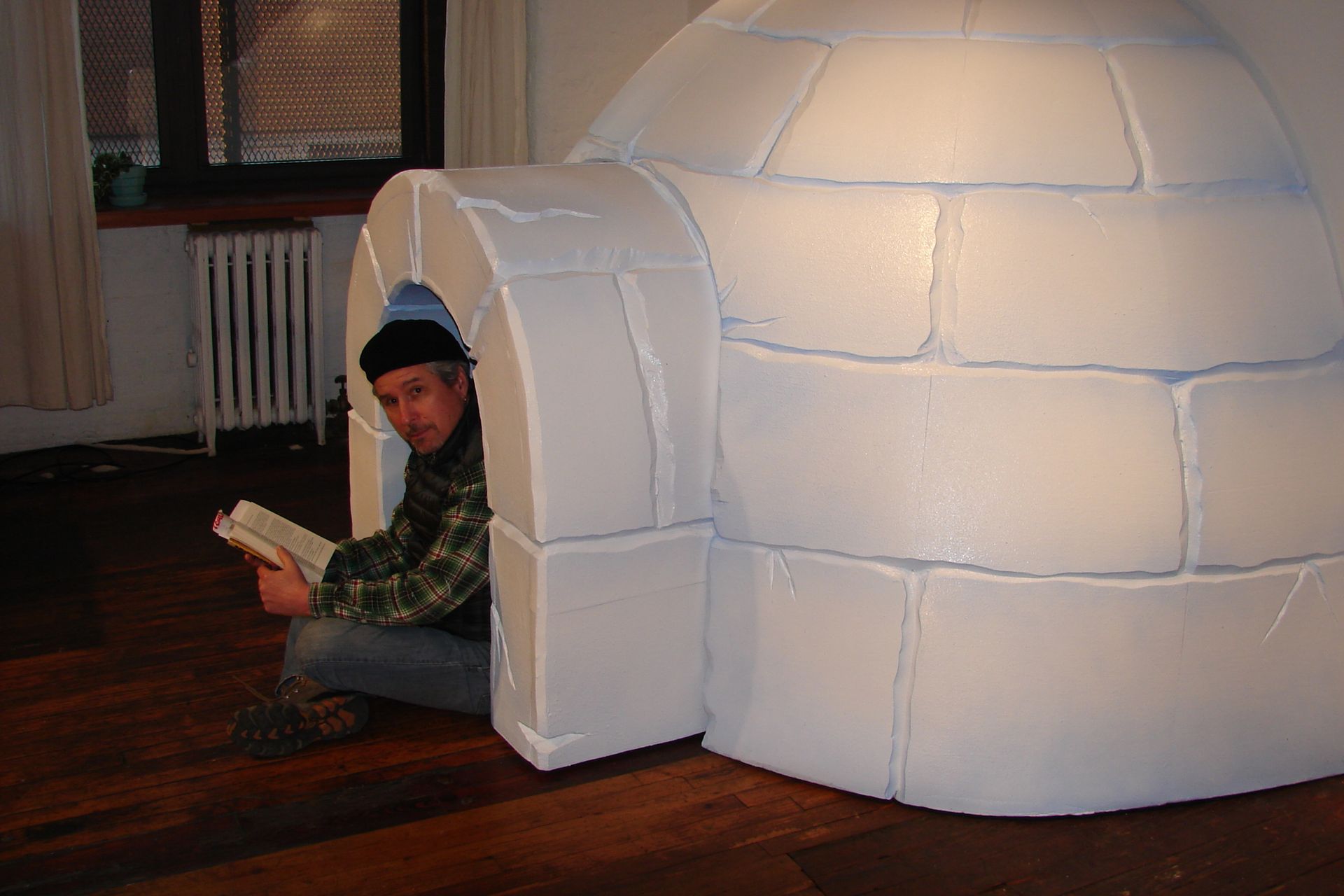 A man is sitting in an igloo reading a book