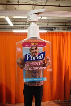 A man is standing in front of a large bottle of purell hand sanitizer.