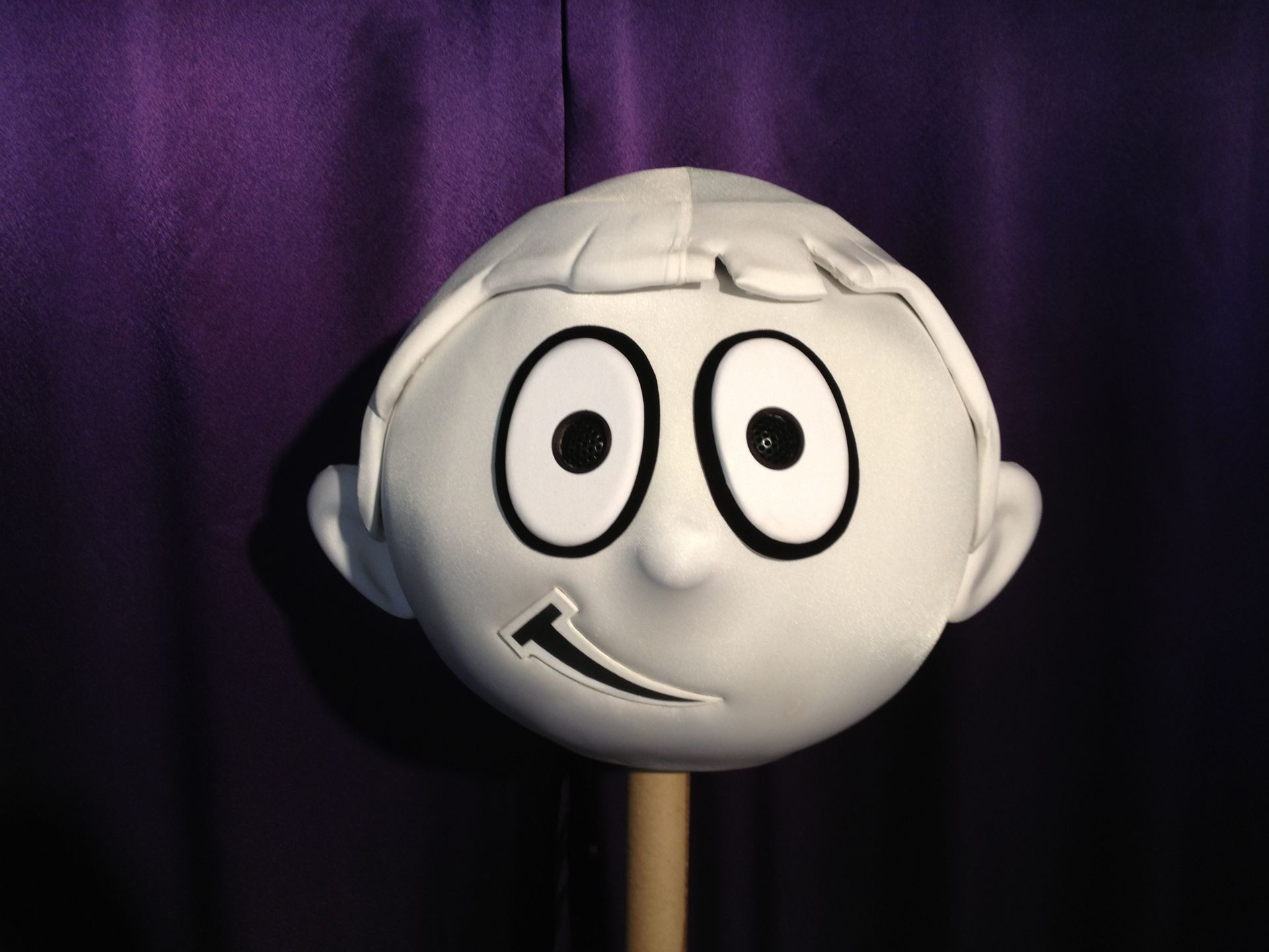 A puppet head with a purple curtain behind it