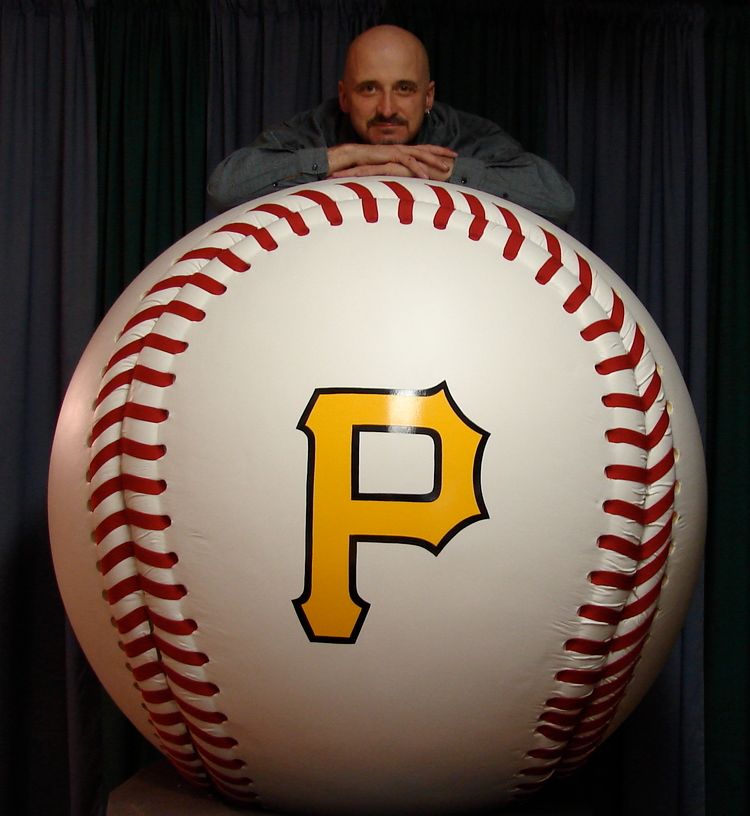 A man leans on a large baseball with the letter p on it
