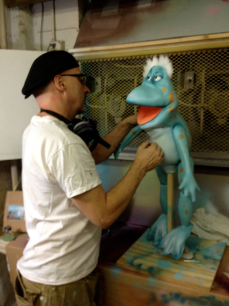 A man is working on a blue frog puppet